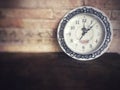 Vintage classic clock on wooden table in front of brick wall. Royalty Free Stock Photo