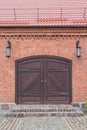 Vintage classic double-sided door in a red brick wall under a tiled roof. Cobblestone walkway and porch in front of a wooden door