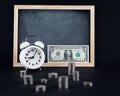 Vintage clock, blackboard, dollar bill, and coin towers on black Royalty Free Stock Photo