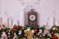 Vintage clock on the mantelpiece. Decor fireplace candles, antique clock and fir branches. Classical fireplace with bronze clocks