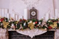 Vintage clock on the mantelpiece. Decor fireplace candles, antique clock and fir branches. Classical fireplace with bronze clocks