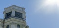 The vintage clock tower on facade of the residential building on blue sky background with sun glare. Urban backgrouund. Royalty Free Stock Photo