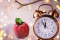 Vintage copper alarm clock showing five minutes to midnight. New Year countdown. Sugar coated red apple ornament hanging on branch Royalty Free Stock Photo