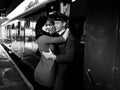 Vintage couple embracing and laughing on railway station platform as train arrives Royalty Free Stock Photo