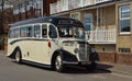 Vintage cream and black Bedford bus being driven along street.