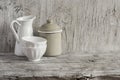 Vintage crockery - enamel jug, enameled jar and white ceramic bowl on bright wooden surface.