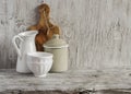 Vintage crockery - enamel jug, enameled jar, white ceramic bowl and olive cutting board on bright wooden surface.