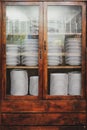 Vintage cupboard with dinnerware. old wooden kitchen cabinet with stack of white plates and cups. retro sideboard