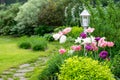 Vintage decorative garden lamp surrounded by blooming tulips, grass, bushes, stone walkway