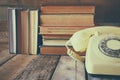 Vintage dial phone next to stack of old books over wooden table Royalty Free Stock Photo