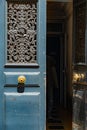 Opened double door with shabby grey blue wooden panels with round brass doorknobs. Old door window with ornate lattice