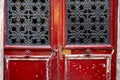 Grunge textures of red shabby wooden door framed panels with vintage ornate black metal gratings in door windows. Royalty Free Stock Photo