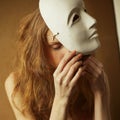 Vintage emotive portrait of a beautiful fashionable red-haired model with a white venetian mask - volto bianco. Close up. Retro