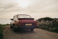 Vintage-filtered photo from low down on the left side of a 1990s classic red sports car with beautiful view of sunset by the sea Royalty Free Stock Photo