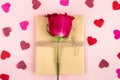 Vintage gift packing in craft paper with twine and one solo pink rose and paper confetti in shape of heart against pink background