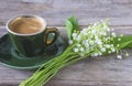 Vintage green cup of coffee and bouquet of lilies of the valley on the old non paint wooden background.