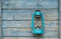 Vintage handle gas lantern on rustic wooden wall. Old fashioned dusty kerosene oil lamp in blue color. Camping light. Interior