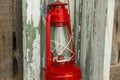 Red vintage handle gas lantern on rustic wooden wall.