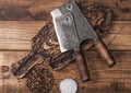 Vintage hatchets for meat on wooden chopping board with salt and pepper on wooden table background. Macro