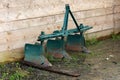 Vintage heavily used rusted agricultural farming equipment in shape of small plow left in muddy backyard in front of wooden boards