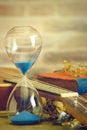 A vintage hourglass and ukulele with an old book and brass pen on a wooden table and brick background in the morning.