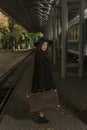 Vintage lady with retro suitcase waiting train at railroad station. Portrait of middle-aged woman in coat and hat Royalty Free Stock Photo