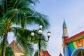 Vintage lamp with a rainbow wall and a tropical palm in amusement park at evening