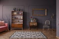 Vintage living room interior with a patterned rug, cupboard, golden frame on the wall, chair and wall molding Royalty Free Stock Photo