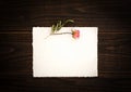 Vintage off-white paper with pretty pink dried rose on dark wood board background table. Paper is blank for your copy, text, word