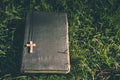 Vintage old holy bible book, grunge textured cover with wooden christian cross. Retro styled image on grass background. Royalty Free Stock Photo