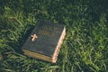 Vintage old holy bible book, grunge textured cover with wooden christian cross. Retro styled image on grass background. Royalty Free Stock Photo