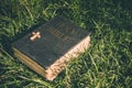 Vintage old holy bible book, grunge textured cover with wooden christian cross. Retro styled image on grass background. Royalty Free Stock Photo