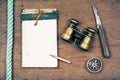 Vintage old notebook, binoculars, compass, knife, rope on wooden table background