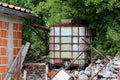 Vintage old partially rusted metal and plastic water container connected to gutter to collect rain water mounted on stone pile and