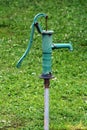 Vintage old rusted green wrought iron hand water pump mounted on single metal pipe in local garden surrounded with uncut grass Royalty Free Stock Photo