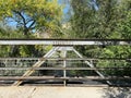 Vintage old steel span bridge walkway over rushing river stream with bright sunlight and shadows Royalty Free Stock Photo