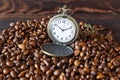 Vintage opened pocket watch among coffee beans on brown wooden table, close-up. Morning coffee,10 o`clock. Royalty Free Stock Photo