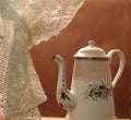 Vintage ornate ceramic teapot beside a white lace curtain