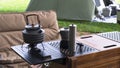 Outdoor black kettle and coffee grinder on camping table with armchair on green lawn in camping area Royalty Free Stock Photo