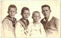 Vintage photo shows the group of four boys (siblings). Some boys wear sailor costume. Black and white portrait. Circa