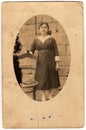 Vintage photo shows woman poses next to historic chair. Antique black white photo is oval shaped.