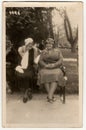 Vintage photo shows women sit on a bench in the city park. Original retro black and white photography.