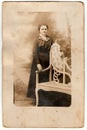 Vintage photo shows young woman poses next to historic carved bench. Black white antique photography.