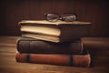 vintage pile of five old brown leather books with eye glasses on a wood table
