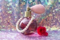 Vintage pink color glass perfume bottle with pearls and red rose blossom on shiny purple sequin texture.