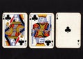 Vintage playing cards showing a run of queen, king and ace of clubs on a black background. Royalty Free Stock Photo