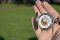 Vintage pocket watch in male hand on a background of green grass. Steampunk watch. Sunny summer day.