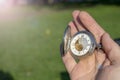 Vintage pocket watch in male hand on a background of green grass. Steampunk watch. Sunny summer day. The clock mechanism is