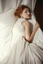 Vintage portrait of a glamorous queen like girl in white dress posing in her bedroom. Perfect hairdo and wild glance. Retro style Royalty Free Stock Photo