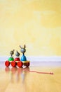 Vintage pull-along wooden toy on a wooden floor against a yellow wall